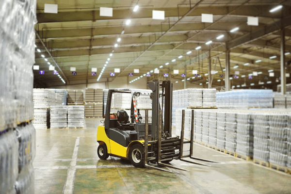 Man operating a forklift indoors loading wooden pallets in a warehouse.
